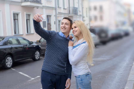 blonde girl and guy doing selfie on city streetの写真素材