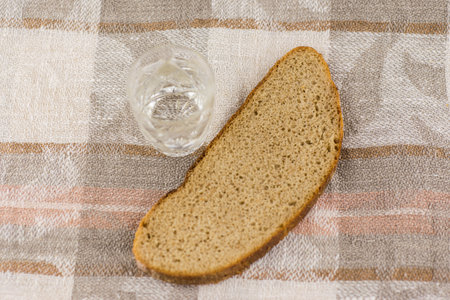 the harmful addiction to alcohol, alcoholism: a Slice of black rye bread lying next to a glass of Russian vodka on a linen woven cloth, top viewの写真素材