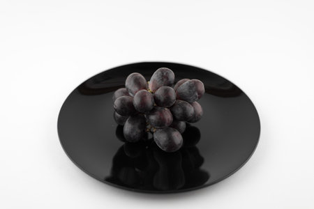 deep red bunch of grapes on black plate, isolated on white backgroundの写真素材