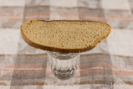 Russian symbol of commemoration of the dead: a loaf of dark rye bread on a full glass of Russian...