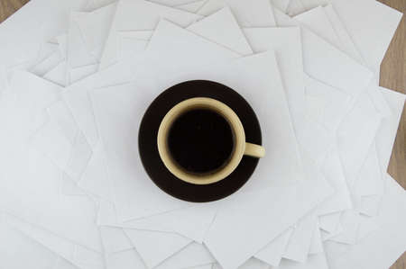 short rest at the hard worker: a Cup of hot coffee and a brown ceramic saucer on a disorderly stack of papersの写真素材