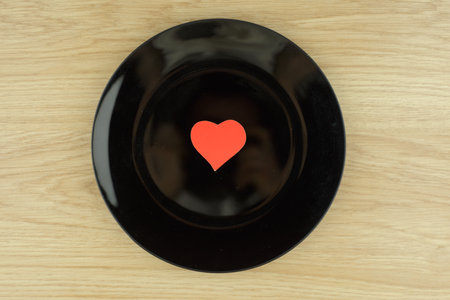 love dish: scarlet heart in the center of the black plate on light wooden table made of oak