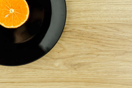 healthy eating vegan: a slice of orange on a black plate in the corner of the wooden table, free space leftの写真素材