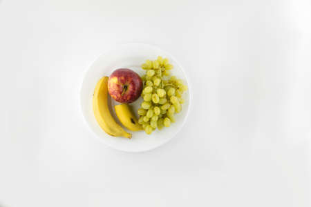 vegetarian diet: still life of grapes, bananas and ripe Apple on a white plate. white backgroundの写真素材