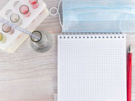 chemical analysis: ballpoint pen next to the Notepad on the background of the test tubes and flasks with a pipette, medical mask, top viewの写真素材