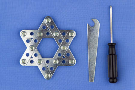 Judaism: star of David, built with meccano, lies on blue fabric with tools, top view