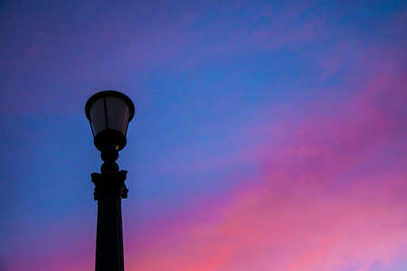 city skyline: the silhouette of an unlit street lamp in the background turning pink sky at dawnの写真素材