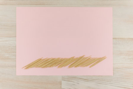 background: a Lot natural bamboo toothpicks laid in a horizontal row on a pink sheet of paperの写真素材
