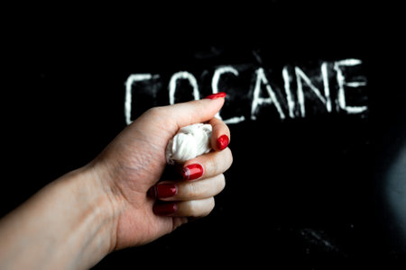 hand squeezes cellophane bag with white powder (drug), the word "cocaine" on a black backgroundの写真素材