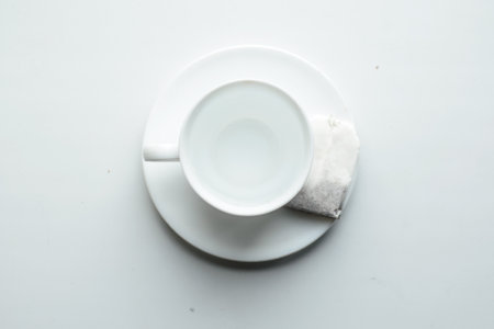 mug full of boiling water on a white saucer and a bag of black loose tea for brewingの写真素材