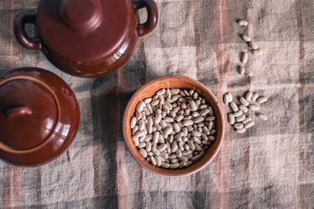 White beans in a clay deep plate on a linen tablecloth among clay pots, soft focusの写真素材