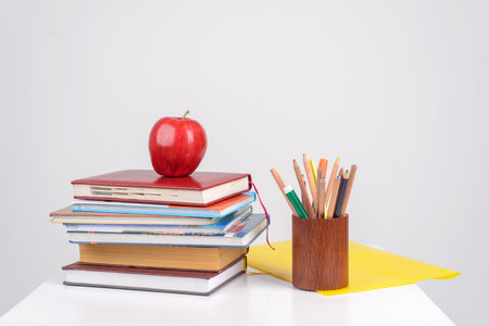 red juicy apple lies on a pile of training books on the table, beside it there are multicolored pencils, pens and markers in the stand and the yellow folder liesの写真素材