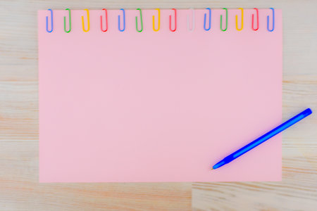 The pink sheet of paper pinned with colored paper clips on the light oak wooden table, with...