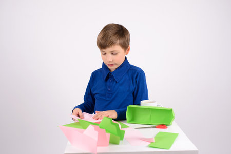 a boy in a blue T-shirt is making origami and drinking tea from a mugの写真素材
