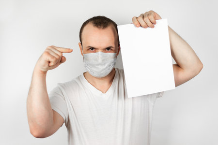 a man in a medical mask points to a white blank sheet of paperの写真素材