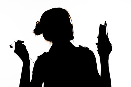 silhouette: a girl in profile, holding a mobile phone, listening to music on the headphones and dancingの写真素材