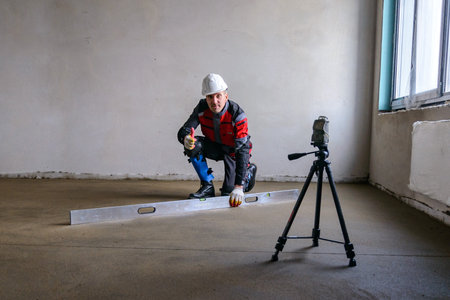A builder in work clothes is doing his job, leveling the floor, pouring mortar