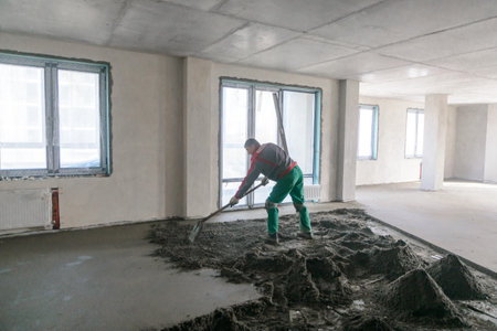 A builder in work clothes is doing his job, leveling the floor, pouring mortarの写真素材