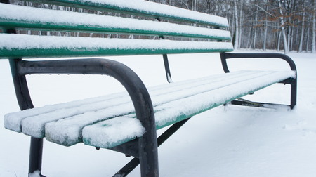 Snow on the bench in winter in park. Tree back ground