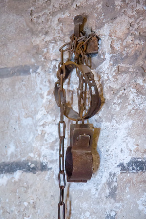 Old rusty shackles with chain on wall in prisonの写真素材