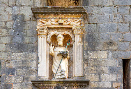 This image shows a historical stone statue set within an ornate niche on a stone wall in Dubrovnik, Croatia.の写真素材