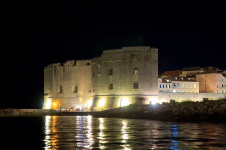 Night view of Dubrovnik, Croatia, with illuminated historic buildings, stone fortress, and light reflections on the Adriatic Sea. Peaceful coastal atmosphere with medieval architecture.の写真素材