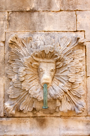ancient stone fountain in Dubrovnik, Croatia, featuring an ornate sculpture of a cow head with a water spout. The intricate carving and historic architecture highlight the city's rich cultural heritage.の写真素材