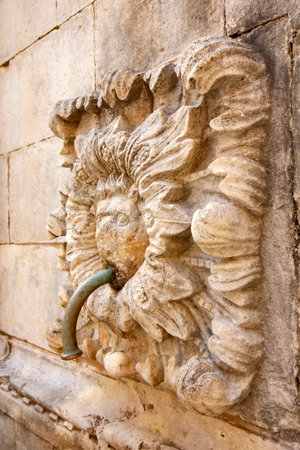 ancient stone fountain in Dubrovnik, Croatia, featuring an ornate sculpture of a cow head with a water spout. The intricate carving and historic architecture highlight the city's rich cultural heritage.の写真素材
