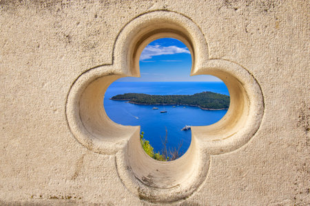 Beautiful scenic view of Dubrovnikâs historic old town and blue Adriatic Sea seen through a stone clover-shaped window on the ancient city walls. Perfect travel and architecture concept.の写真素材