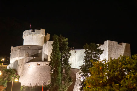 Night view of Dubrovnik, Croatia, with illuminated historic buildings, stone fortress, and light reflections on the Adriatic Sea. Peaceful coastal atmosphere with medieval architecture.の写真素材