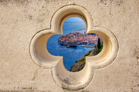 Beautiful scenic view of Dubrovnikâs historic old town and blue Adriatic Sea seen through a stone clover-shaped window on the ancient city walls. Perfect travel and architecture concept.の写真素材