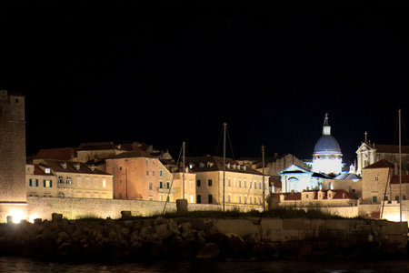 Night view of Dubrovnik, Croatia, with illuminated historic buildings, stone fortress, and light reflections on the Adriatic Sea. Peaceful coastal atmosphere with medieval architecture.の写真素材