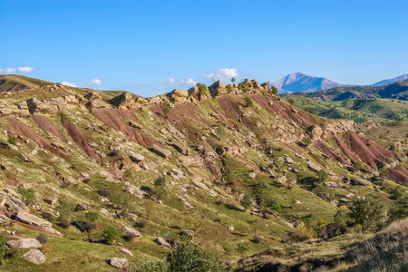 Layered rock formations of the Zagros Mountains, featuring distinctive red and green sedimentary strata under a clear sky in Kurdistanの写真素材