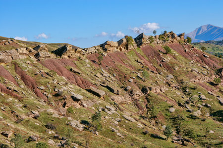Layered rock formations of the Zagros Mountains, featuring distinctive red and green sedimentary strata under a clear sky in Kurdistanの写真素材