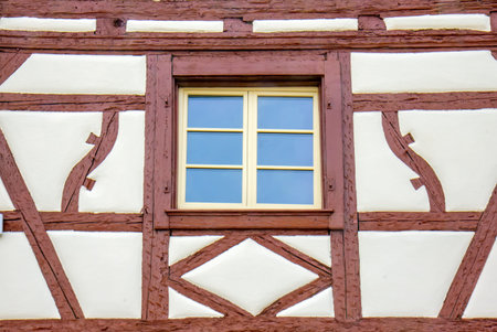 Historic timber framed wall with old window and weathered shutters in traditional Colmar architecture.の写真素材