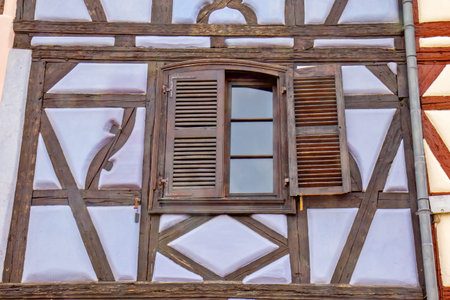 Historic timber framed wall with old window and weathered shutters in traditional Colmar architecture.の写真素材