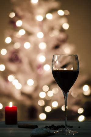 Wine glass on a table decorated with candle and cookies  Defocused lights on a white Christmas tree in background の写真素材
