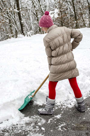 Young woman shoveling snow off street with green shovel の写真素材