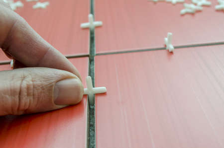 Closeup of tilers hand while using spacer for installing a red ceramic tiles on the floor の写真素材