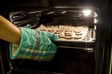 Taking baked cookies out of the oven with kitchen gloves  の写真素材