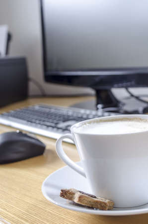 A cup of coffee on a wooden office desk with computer in background の写真素材