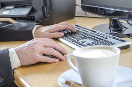 A man working at the office desk with a blurred coffee in front の写真素材