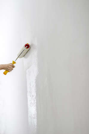 Female hand painting white wall with paint roller の写真素材