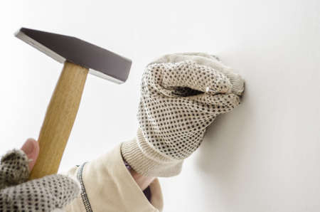 Worker in gloves hammering a nail into white wall の写真素材