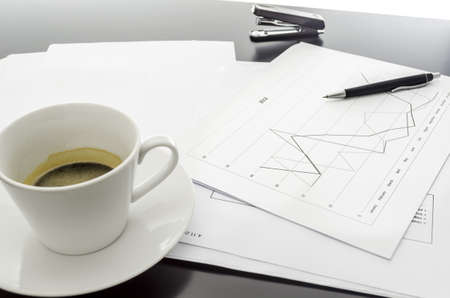 Side view of a graph document, coffee and a pen on a black office desk の写真素材