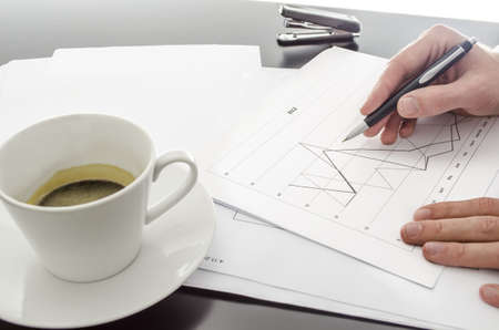 Male hand holding a pen over a business document on a black office desk の写真素材