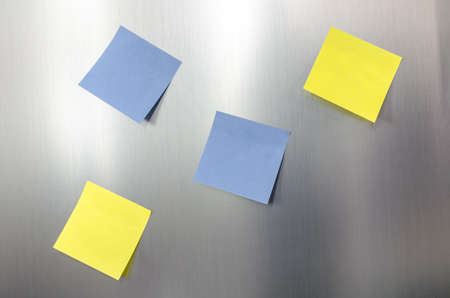 Four blank sticky note reminders on a stainless fridge の写真素材