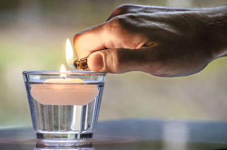 Hand with a lighter lighting a candle floating in water 