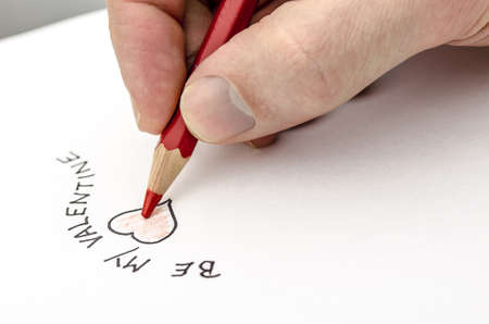Male hand writing a Be my Valentine note on a white paper の写真素材