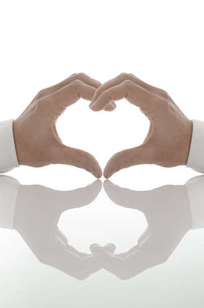 Heart shape of two hands with reflection on a white table の写真素材